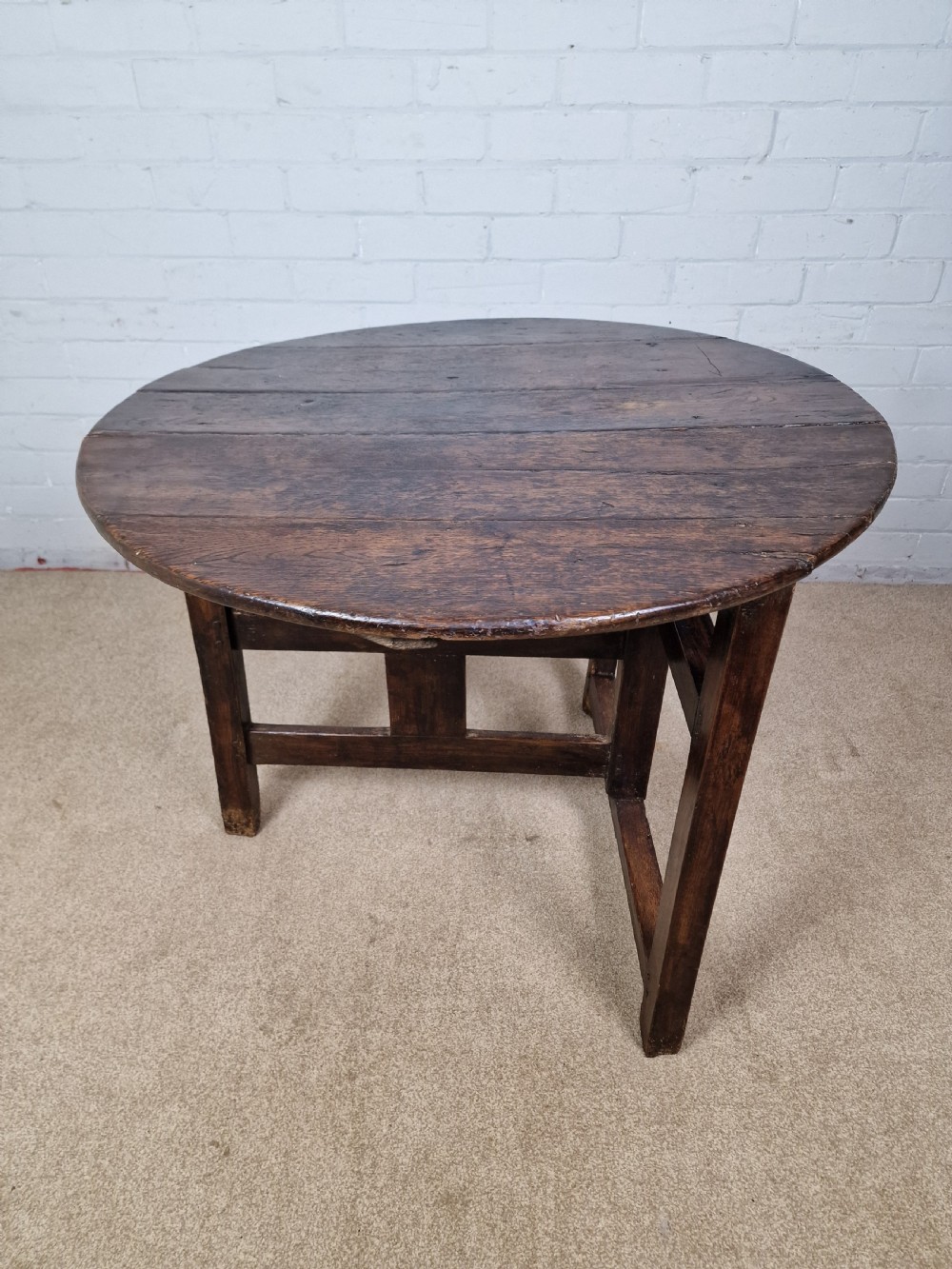 A circular dark oak George III coaching table featuring a planked top and a folding wooden base structure. View III