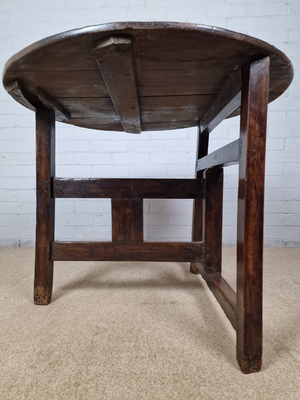 A circular dark oak George III coaching table featuring a planked top and a folding wooden base structure. View IV