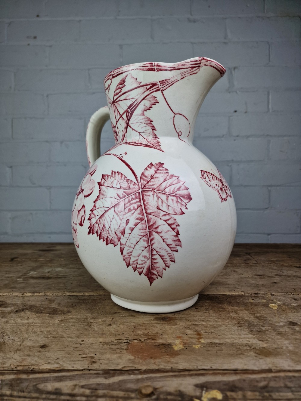 A Victorian cream ceramic jug decorated with a red transferware pattern of grapes and vine leaves. View IV
