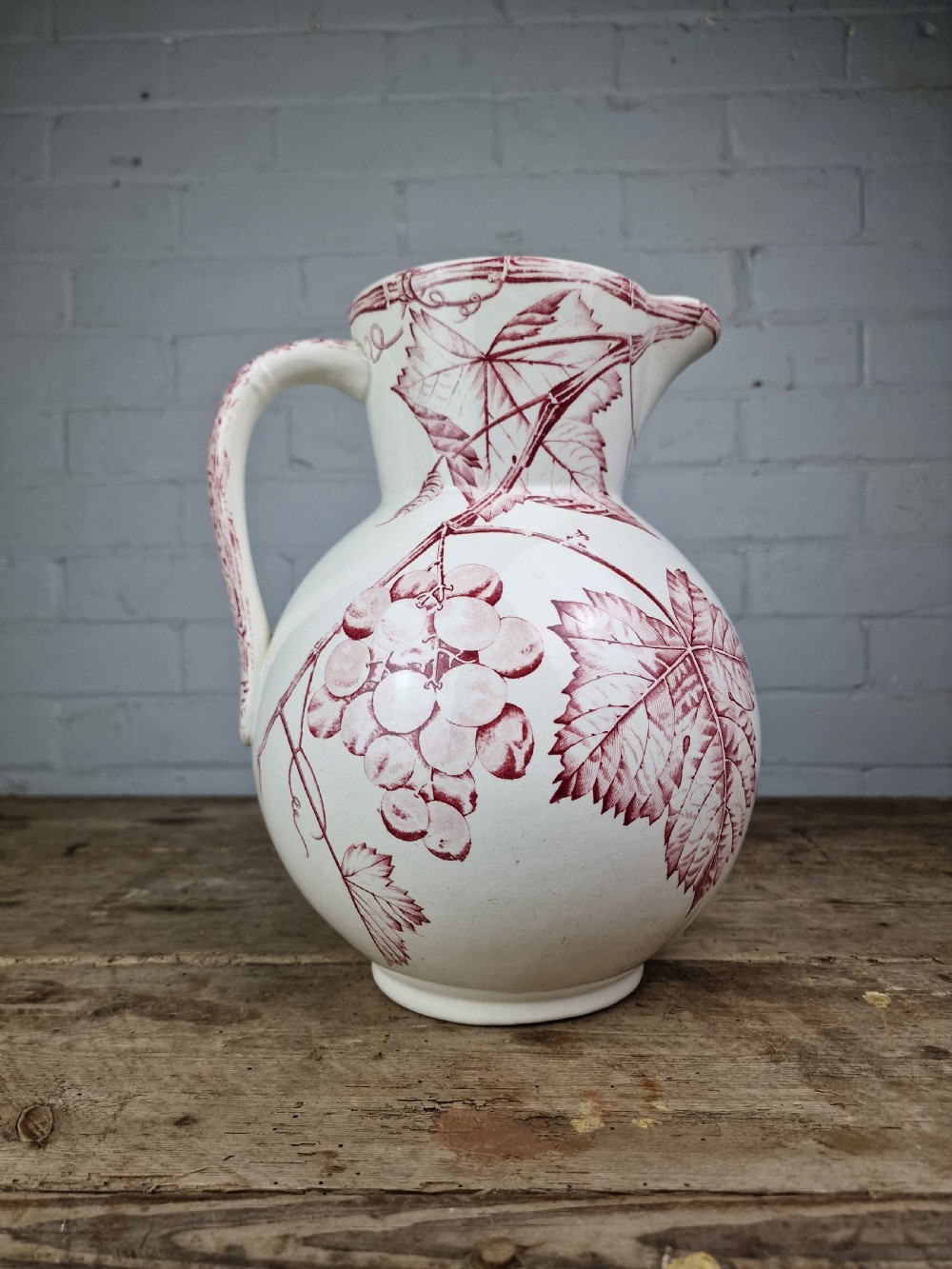 A Victorian cream ceramic jug decorated with a red transferware pattern of grapes and vine leaves. View V