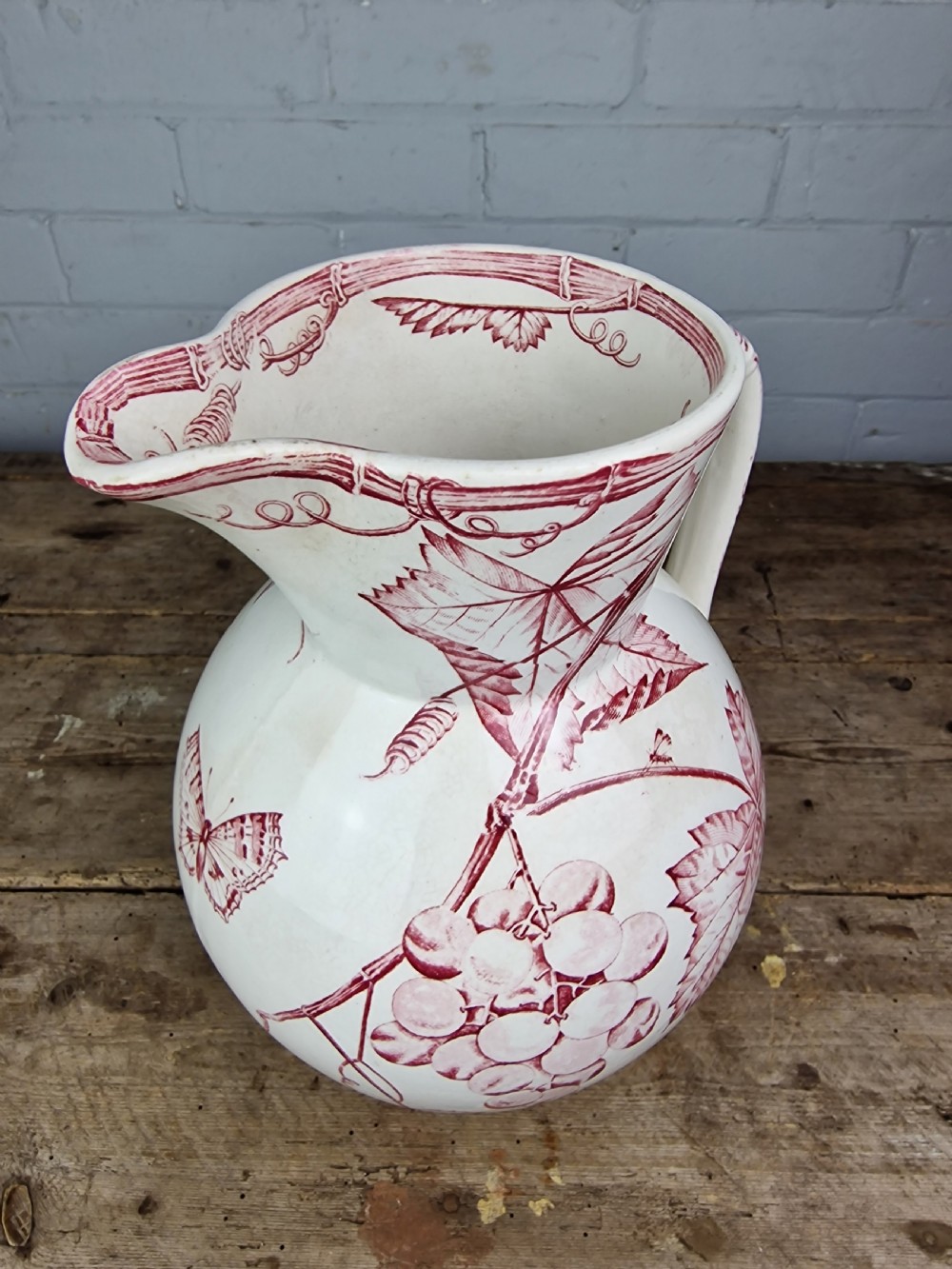 A Victorian cream ceramic jug decorated with a red transferware pattern of grapes and vine leaves. View X