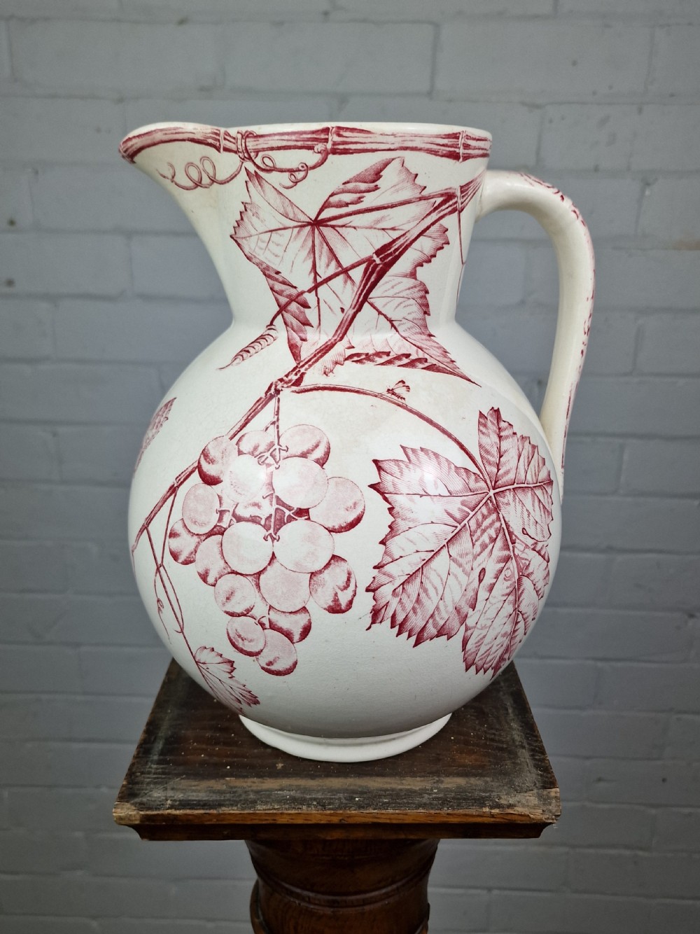 A Victorian cream ceramic jug decorated with a red transferware pattern of grapes and vine leaves.