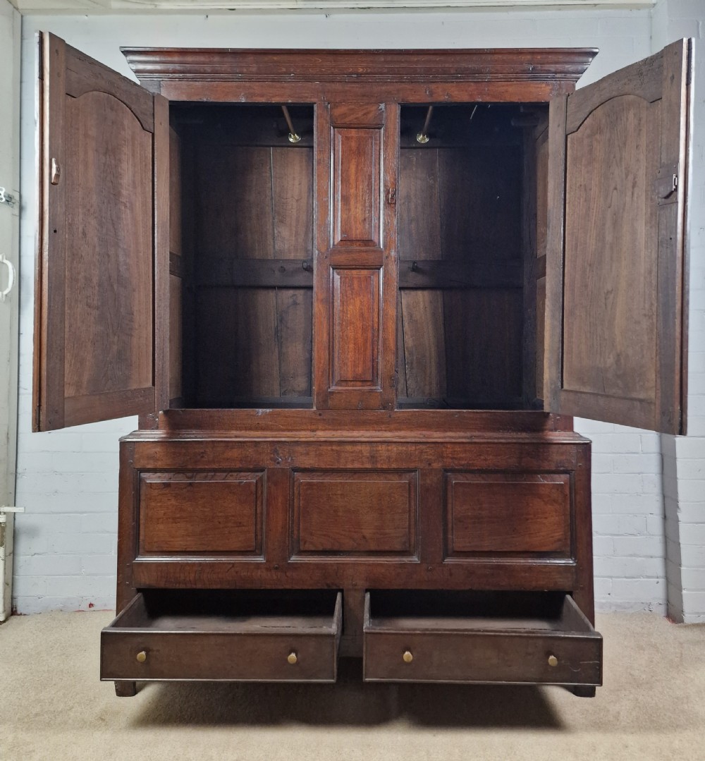 A tall Georgian dark oak livery cupboard featuring arched panel doors, iron hinges, three lower panels, and two drawers at the base. View II