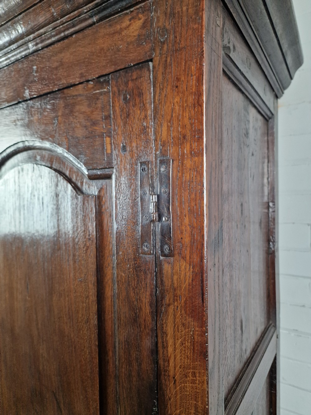 A tall Georgian dark oak livery cupboard featuring arched panel doors, iron hinges, three lower panels, and two drawers at the base. View IV