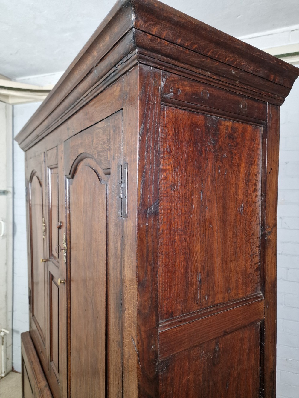 A tall Georgian dark oak livery cupboard featuring arched panel doors, iron hinges, three lower panels, and two drawers at the base. View VIII
