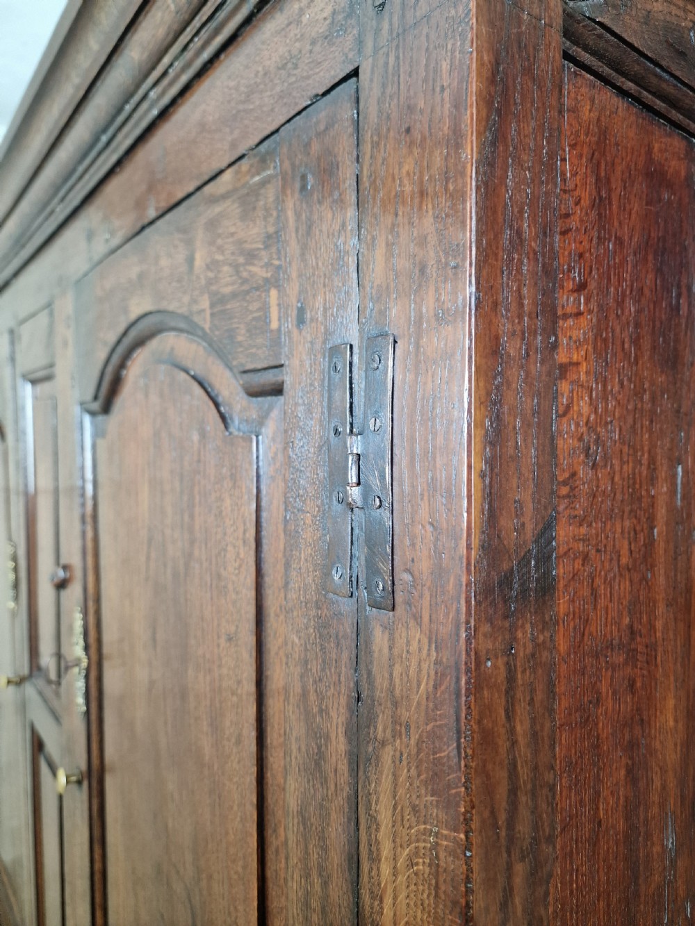 A tall Georgian dark oak livery cupboard featuring arched panel doors, iron hinges, three lower panels, and two drawers at the base. View IX