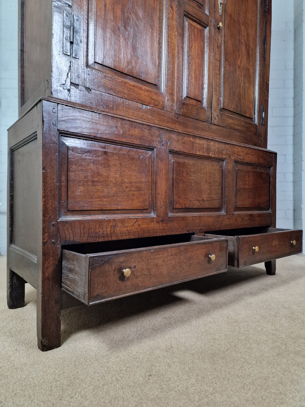 A tall Georgian dark oak livery cupboard featuring arched panel doors, iron hinges, three lower panels, and two drawers at the base. View XII