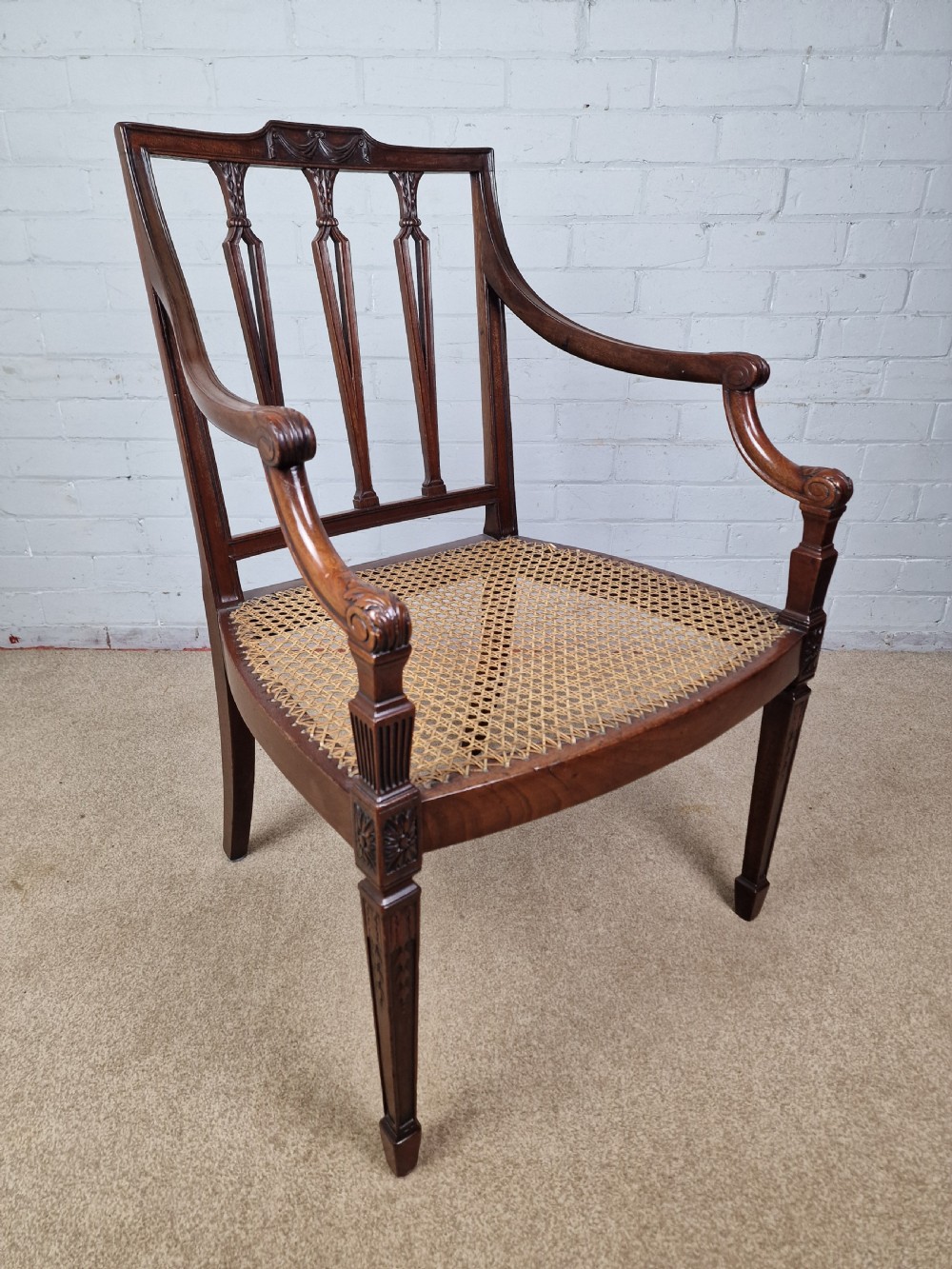 A Georgian mahogany open armchair featuring carved splats, curved arms, tapered fluted front legs, and a padded blue velvet cushion seat. View X