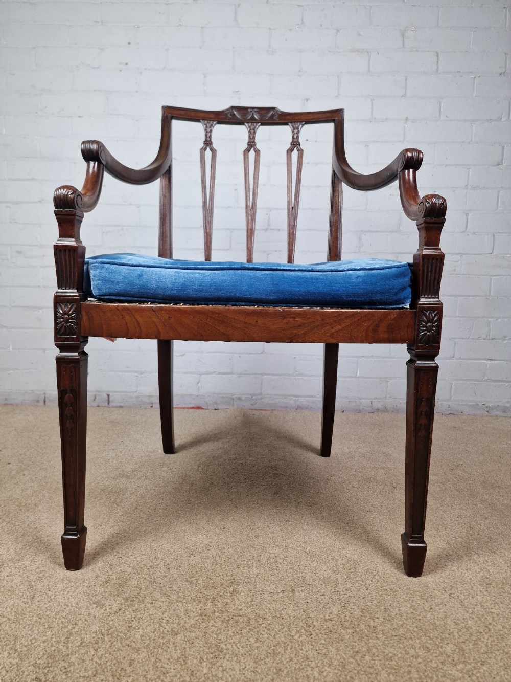 A Georgian mahogany open armchair featuring carved splats, curved arms, tapered fluted front legs, and a padded blue velvet cushion seat. View XII