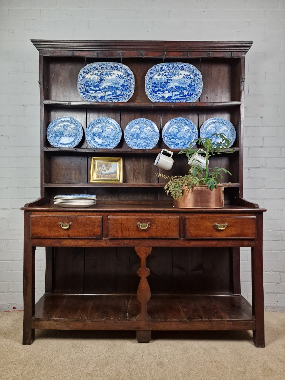 An 18th-century George II oak dresser featuring a top open plate rack above three frieze drawers and an open lower pot shelf.