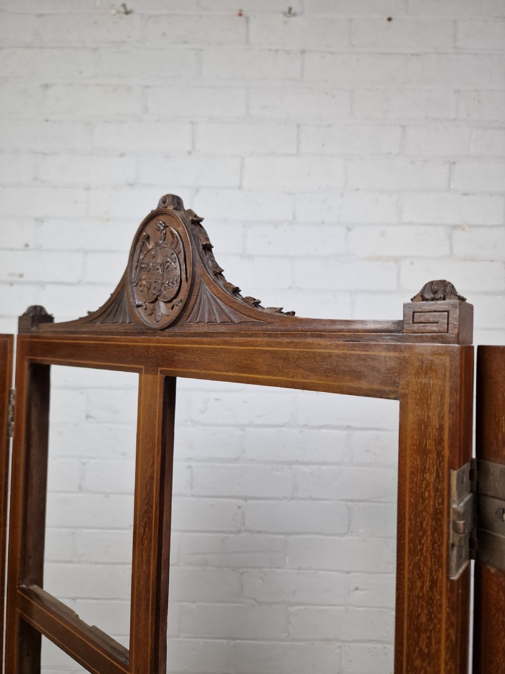 An Edwardian three-panel mahogany folding screen featuring a central carved crest, glazed grid panes, and bracket feet. View V
