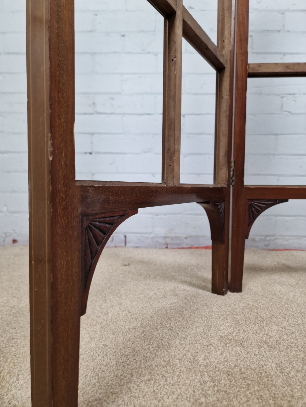 An Edwardian three-panel mahogany folding screen featuring a central carved crest, glazed grid panes, and bracket feet. View VI