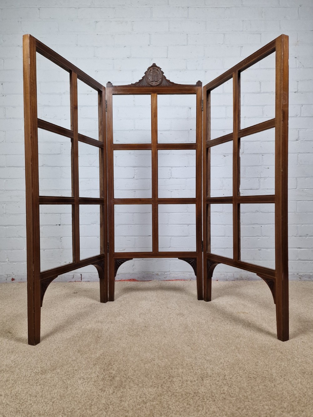 An Edwardian three-panel mahogany folding screen featuring a central carved crest, glazed grid panes, and bracket feet. View VII