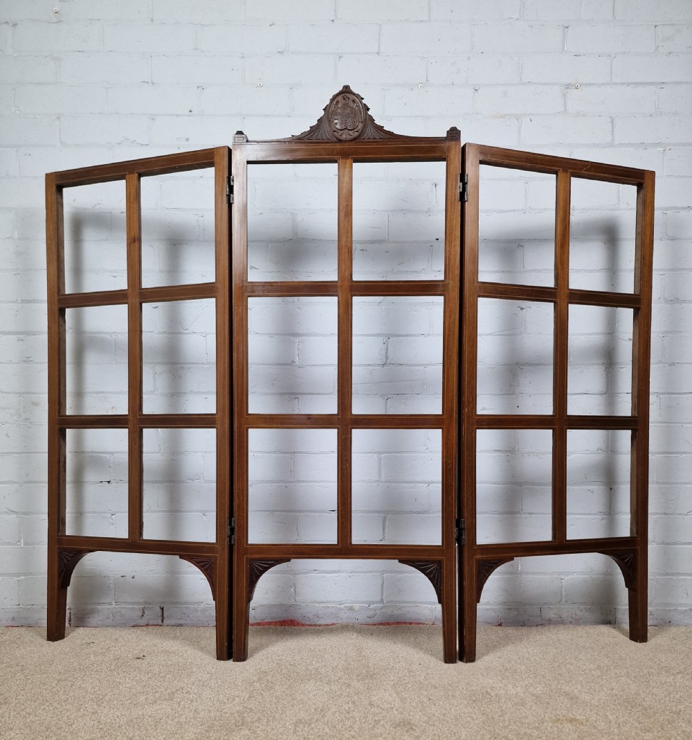 An Edwardian three-panel mahogany folding screen featuring a central carved crest, glazed grid panes, and bracket feet. View VIII