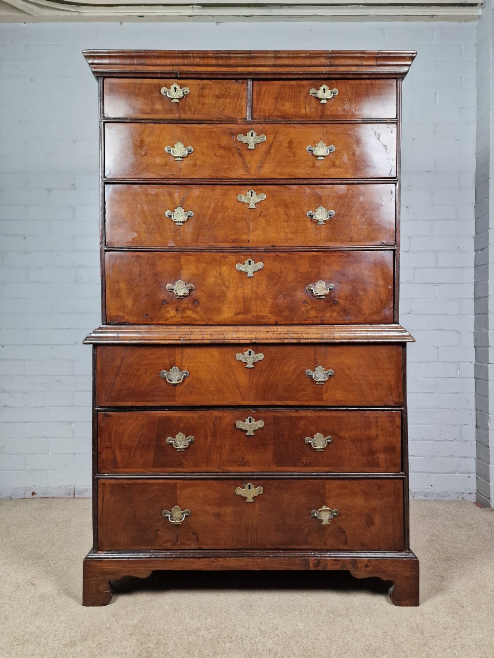 An early eighteenth-century Georgian walnut secretaire chest on chest featuring brass drop handles, a drop-front desk compartment with fitted pigeonholes, and bracket feet. View VI