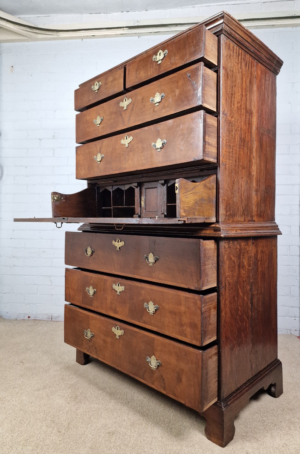An early eighteenth-century Georgian walnut secretaire chest on chest featuring brass drop handles, a drop-front desk compartment with fitted pigeonholes, and bracket feet. View V