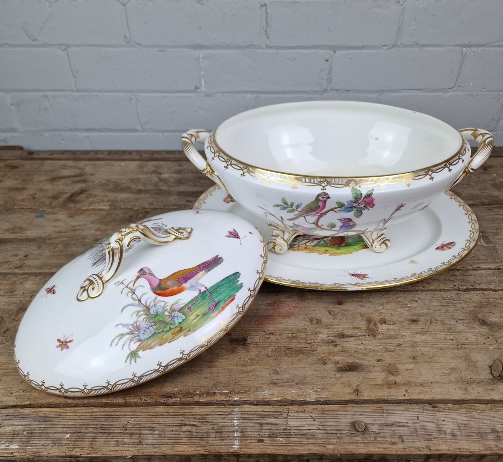 An antique white porcelain soup tureen featuring hand-painted bird motifs, gilded scroll handles, four scroll feet, and a matching underplate. View II