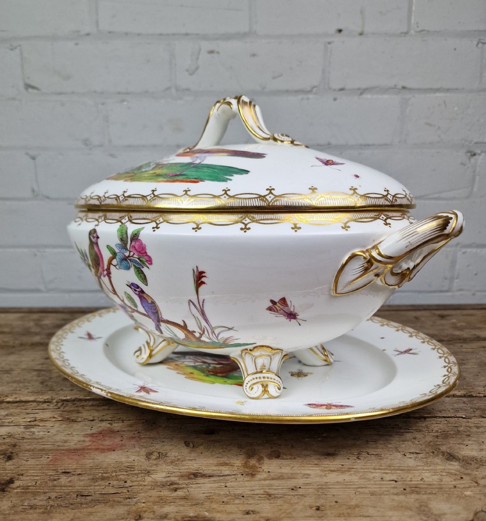 An antique white porcelain soup tureen featuring hand-painted bird motifs, gilded scroll handles, four scroll feet, and a matching underplate. View VI
