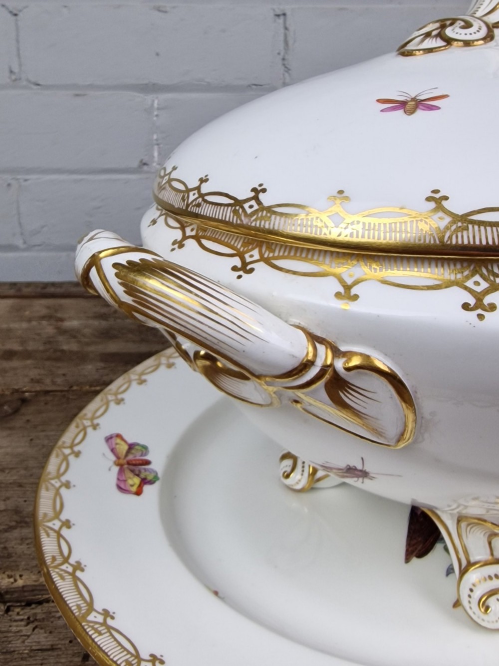 An antique white porcelain soup tureen featuring hand-painted bird motifs, gilded scroll handles, four scroll feet, and a matching underplate. View VIII