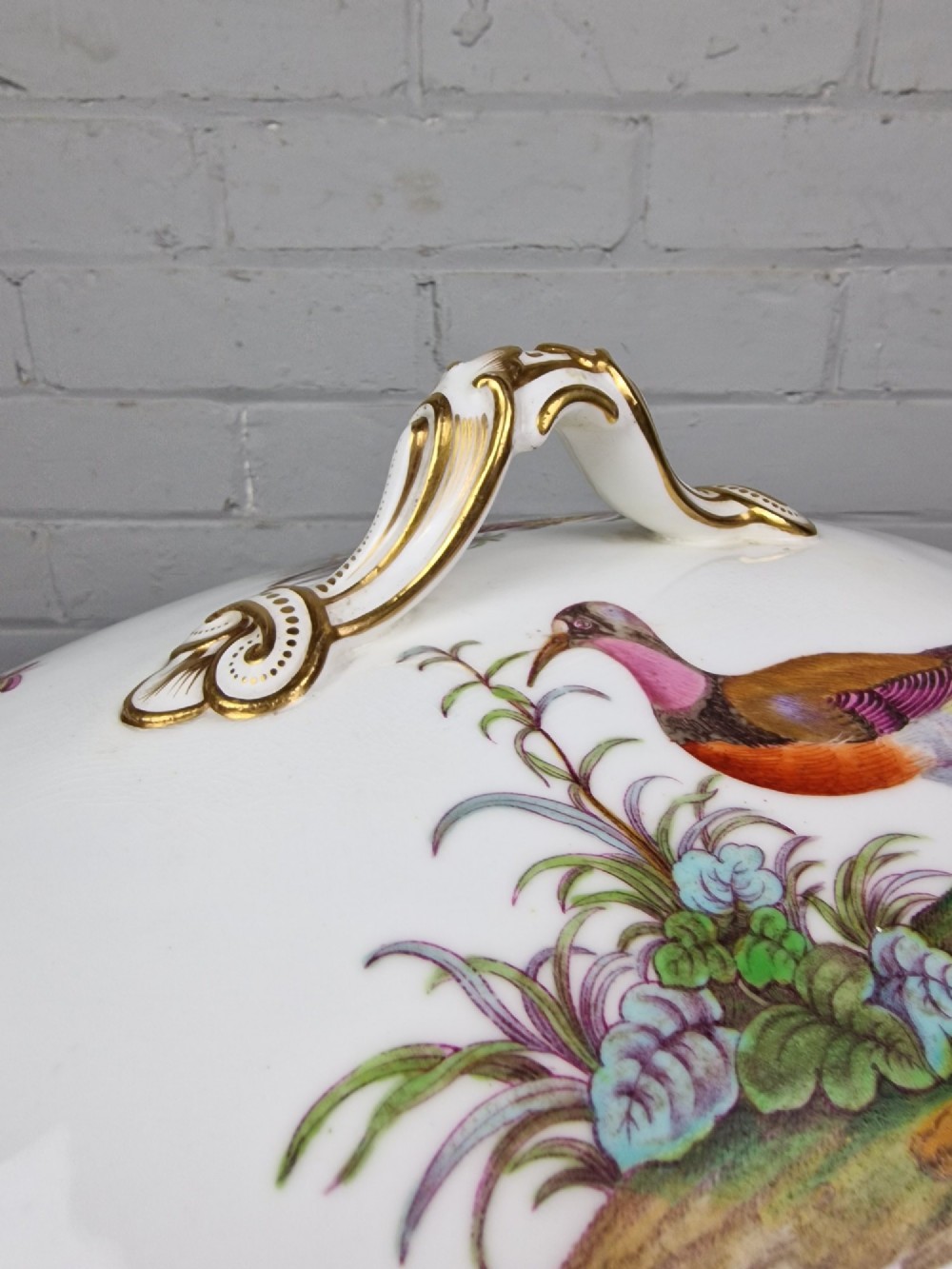 An antique white porcelain soup tureen featuring hand-painted bird motifs, gilded scroll handles, four scroll feet, and a matching underplate. View IX