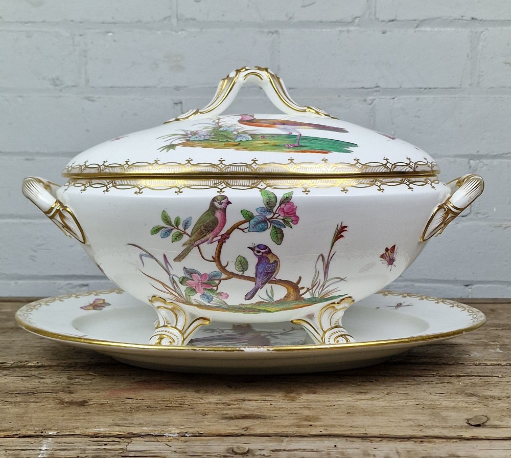 An antique white porcelain soup tureen featuring hand-painted bird motifs, gilded scroll handles, four scroll feet, and a matching underplate. View X