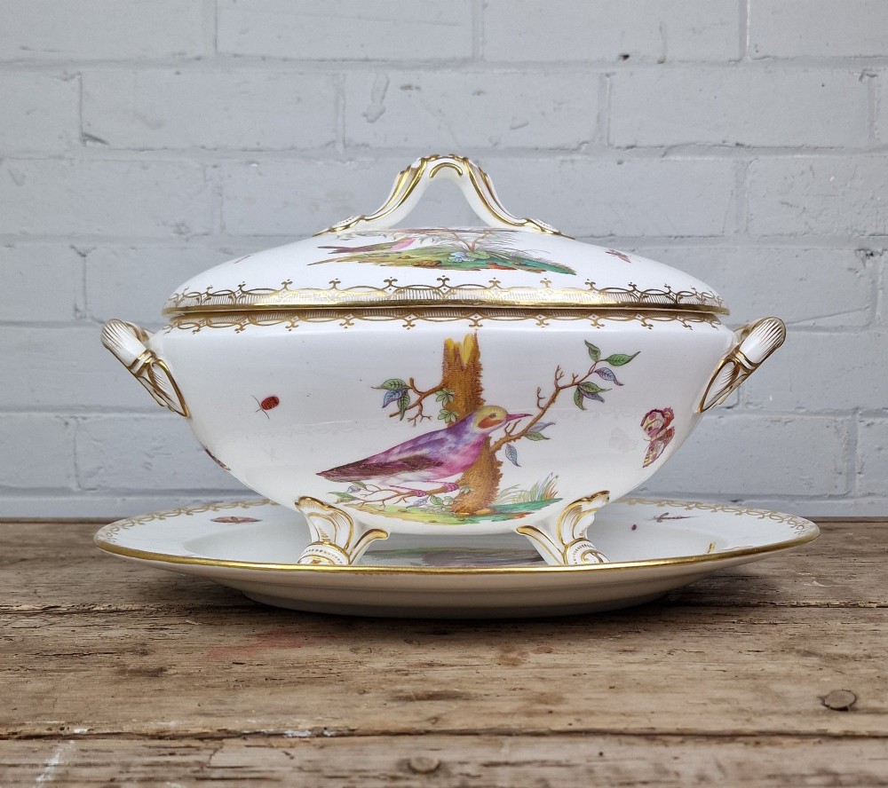 An antique white porcelain soup tureen featuring hand-painted bird motifs, gilded scroll handles, four scroll feet, and a matching underplate. View XI