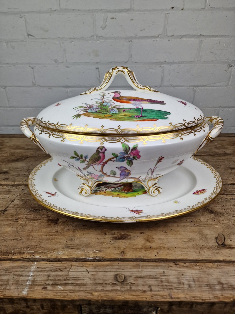 An antique white porcelain soup tureen featuring hand-painted bird motifs, gilded scroll handles, four scroll feet, and a matching underplate. View XV