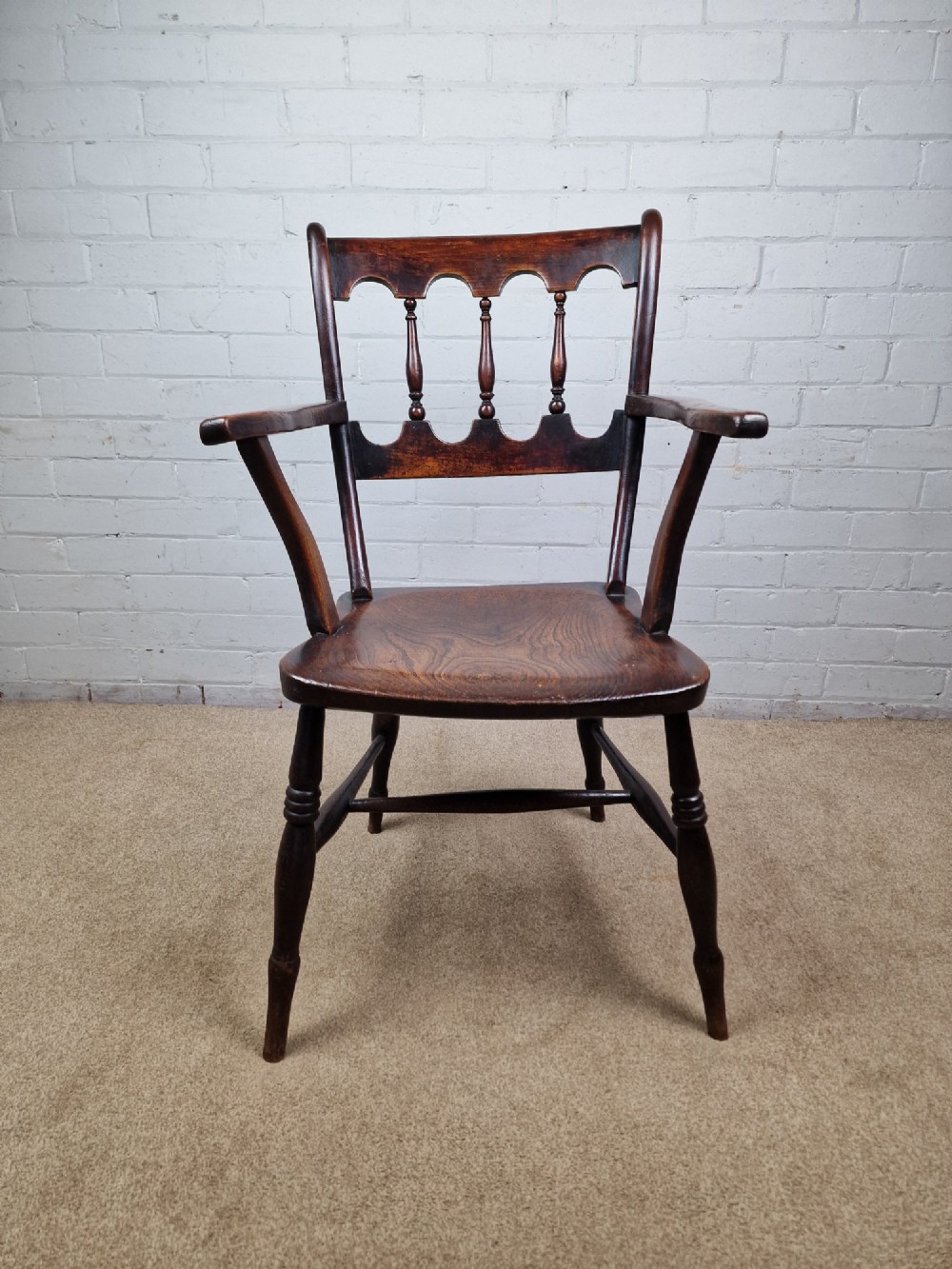 A Victorian dark brown elm and beech Oxford bar back Windsor armchair featuring turned spindles, shaped armrests, and turned legs with stretchers.