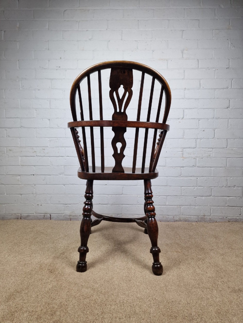 A 19th-century low-back wooden Windsor armchair featuring a curved top rail, pierced central splat, vertical spindles, turned legs, and a crinoline stretcher. View V