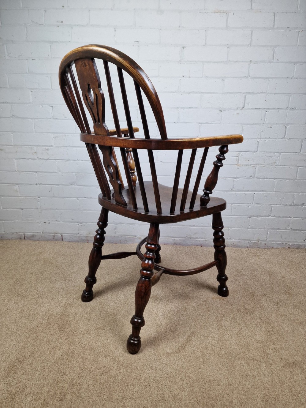A 19th-century low-back wooden Windsor armchair featuring a curved top rail, pierced central splat, vertical spindles, turned legs, and a crinoline stretcher. View VI