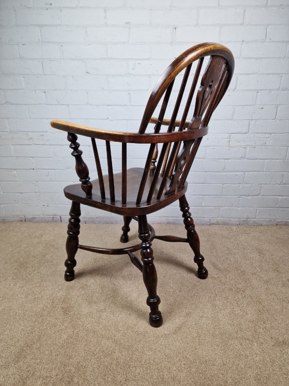 A 19th-century low-back wooden Windsor armchair featuring a curved top rail, pierced central splat, vertical spindles, turned legs, and a crinoline stretcher. View VII