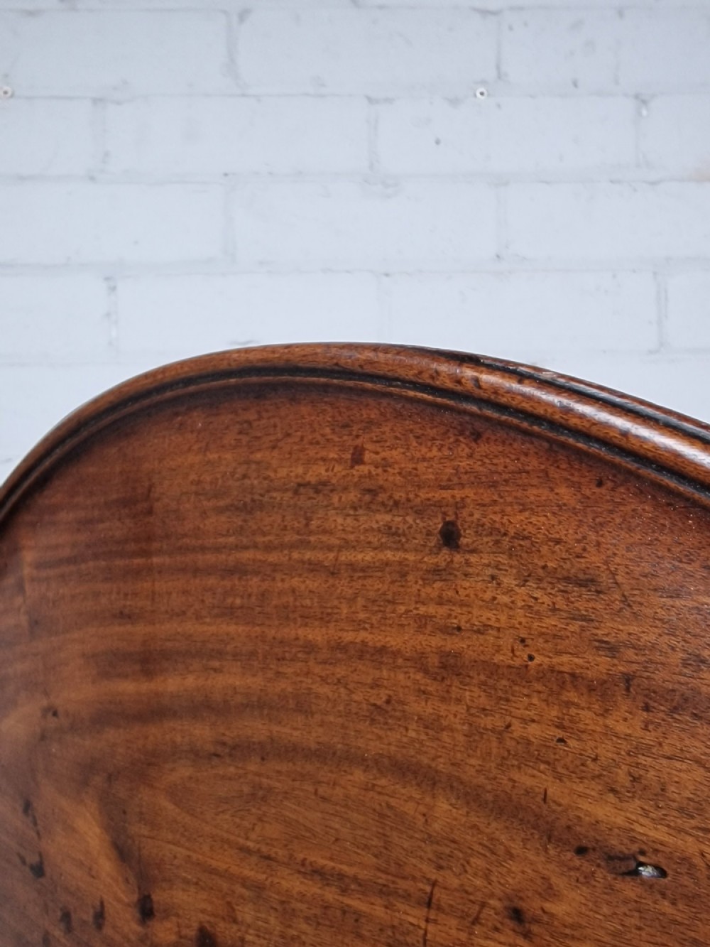 A late eighteenth-century Georgian mahogany tripod table shown with its circular dished top tilted vertically above a turned baluster pedestal on three cabriole legs. View II