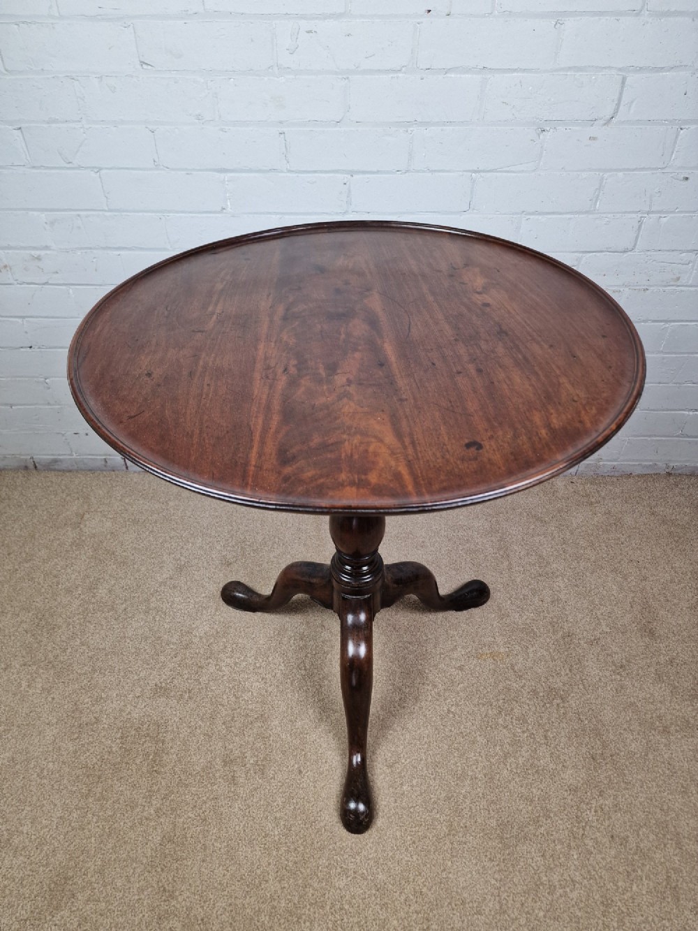 A late eighteenth-century Georgian mahogany tripod table shown with its circular dished top tilted vertically above a turned baluster pedestal on three cabriole legs. View V