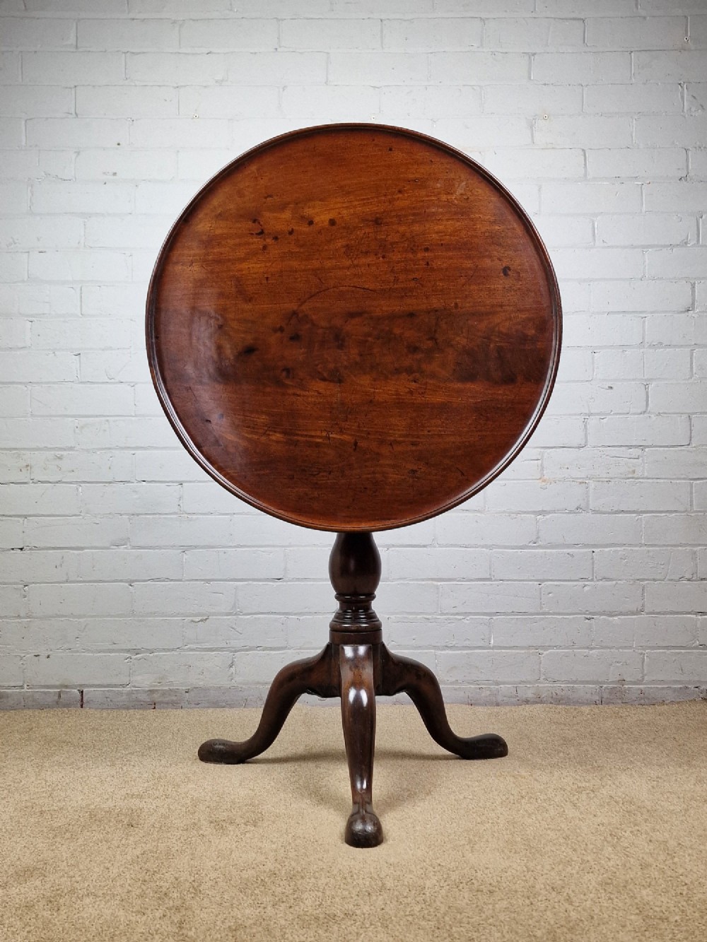 A late eighteenth-century Georgian mahogany tripod table shown with its circular dished top tilted vertically above a turned baluster pedestal on three cabriole legs.