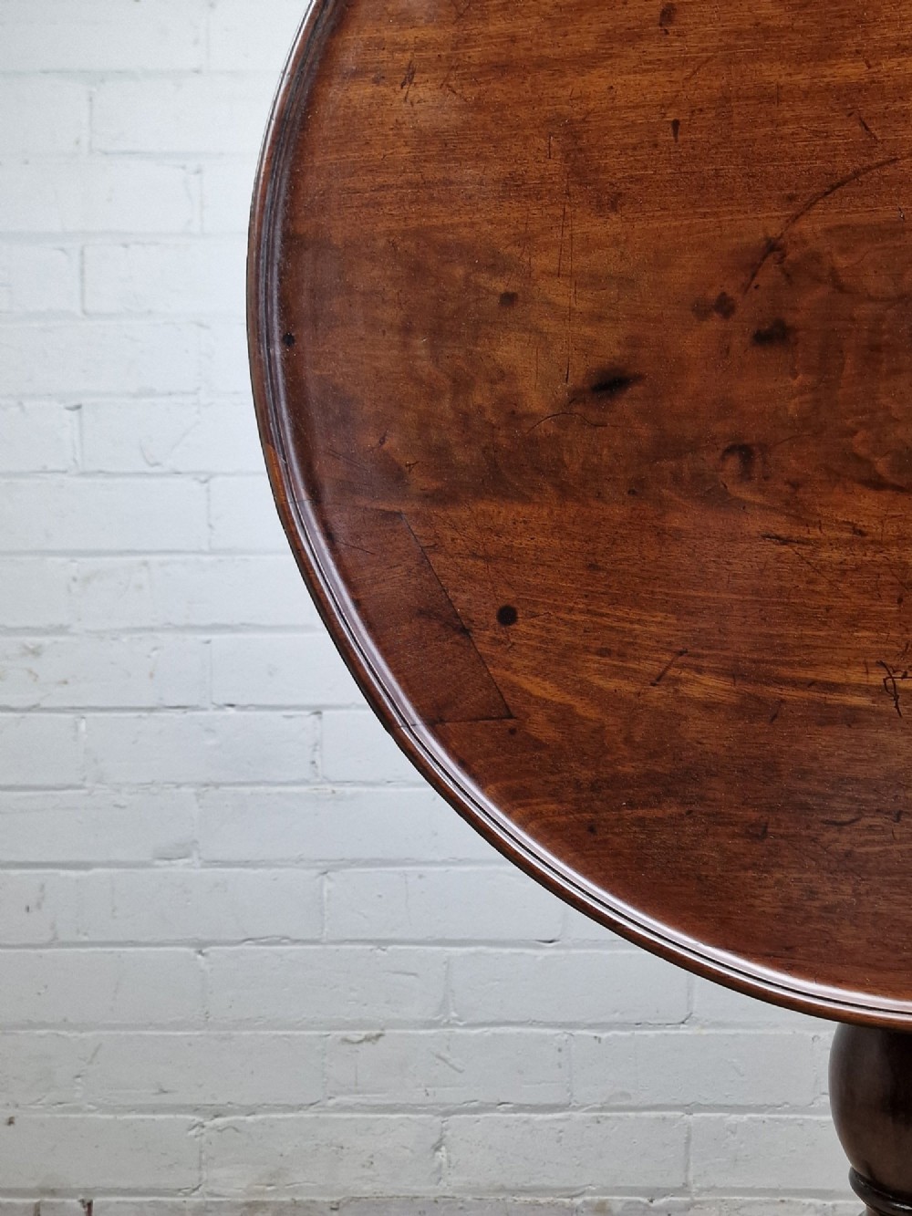 A late eighteenth-century Georgian mahogany tripod table shown with its circular dished top tilted vertically above a turned baluster pedestal on three cabriole legs. View IX