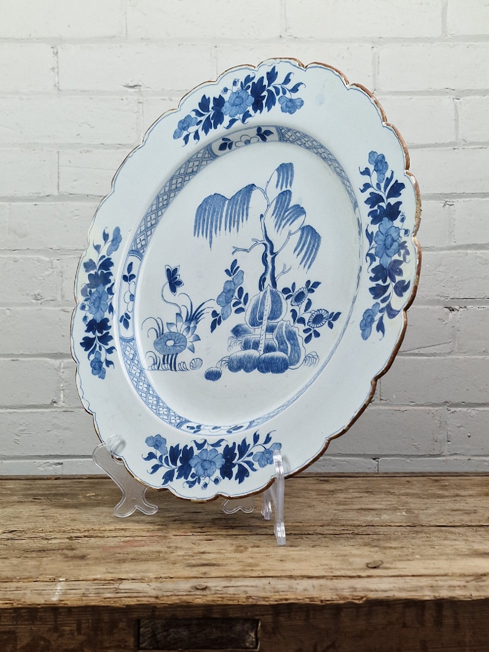 An 18th-century English Delftware charger featuring cobalt blue chinoiserie landscape hand-painted on a white scalloped earthenware platter. View II