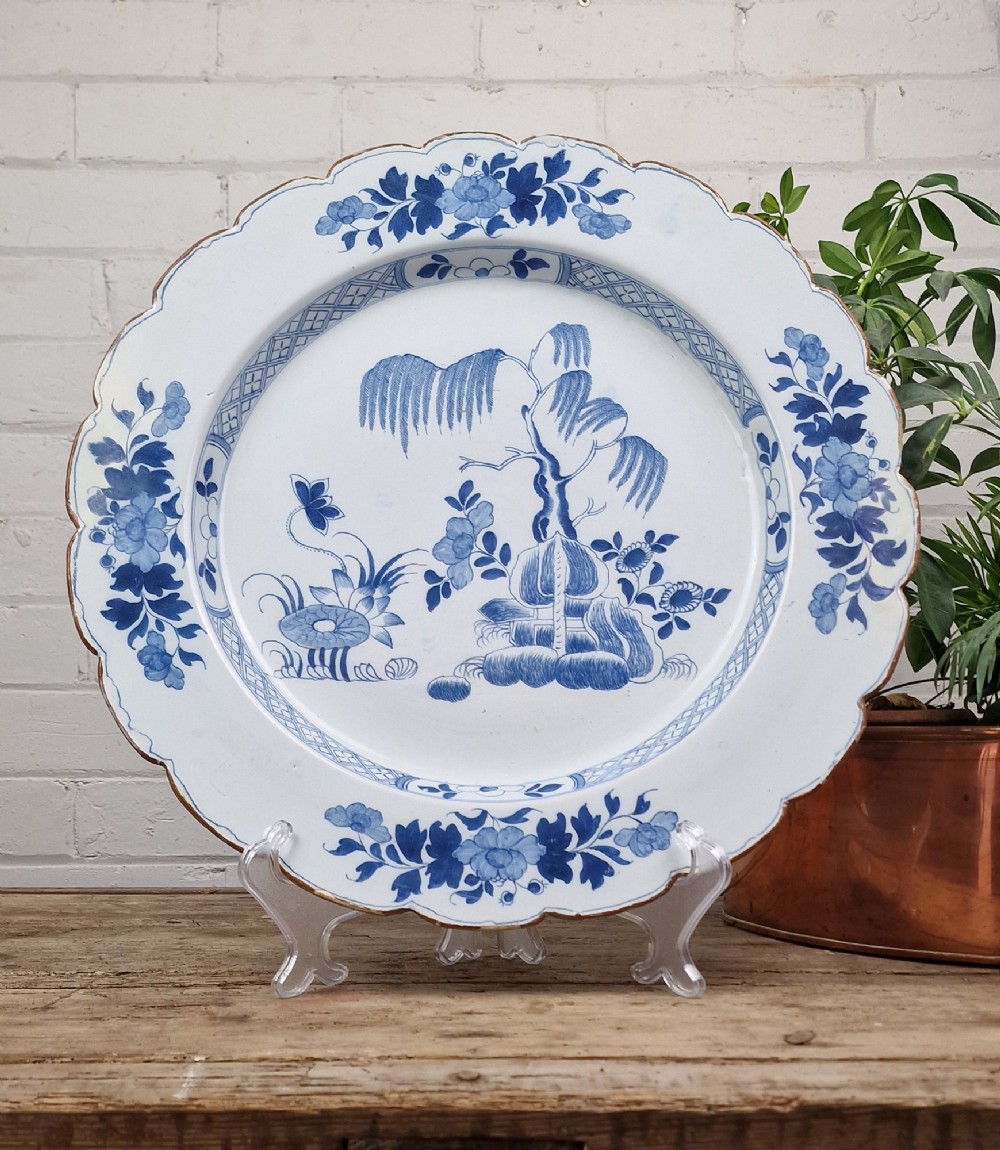 An 18th-century English Delftware charger featuring cobalt blue chinoiserie landscape hand-painted on a white scalloped earthenware platter.