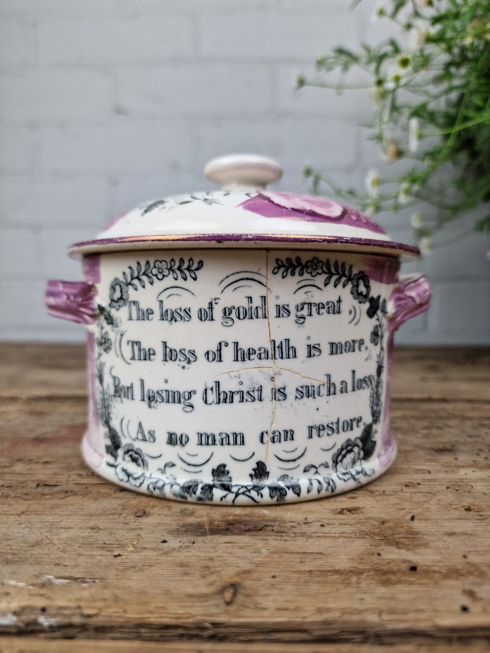 A cream earthenware butter dish with pink splash lustre accents, side handles, and a black transfer print depicting a bridge over a river. View II