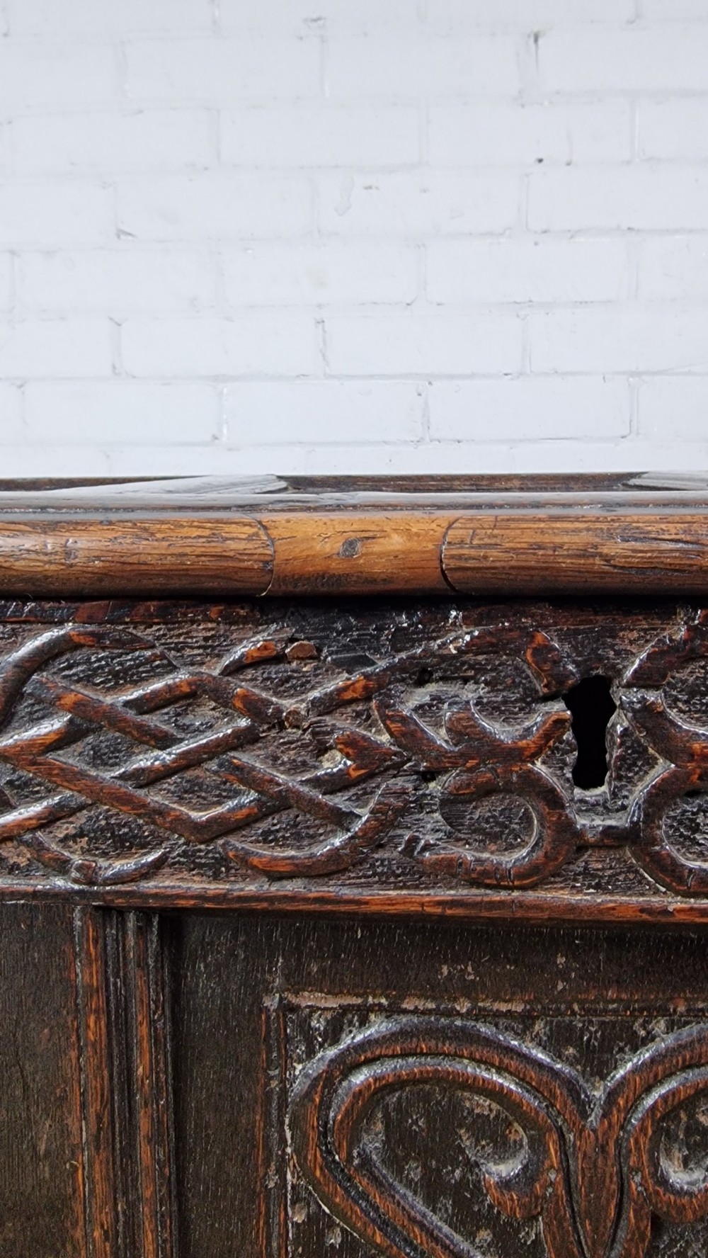 A late 17th-century dark oak coffer with a hinged lid, featuring three carved front panels and an intricate carved top frieze. View II