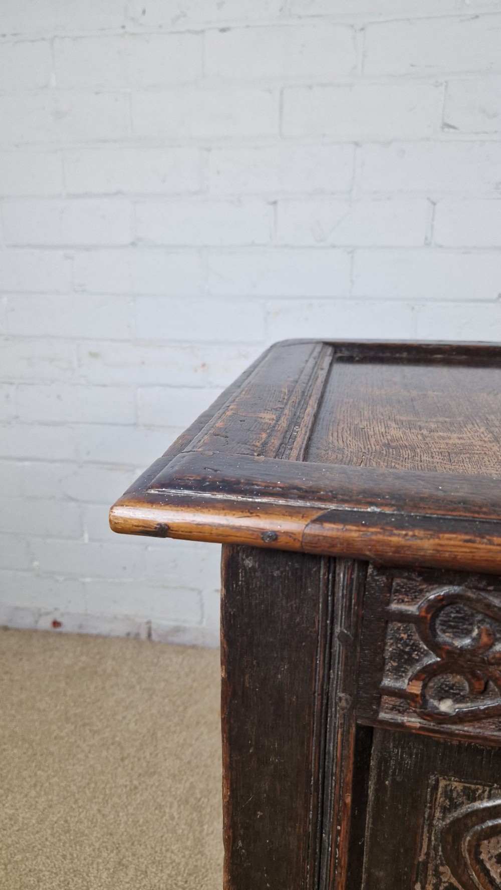 A late 17th-century dark oak coffer with a hinged lid, featuring three carved front panels and an intricate carved top frieze. View III