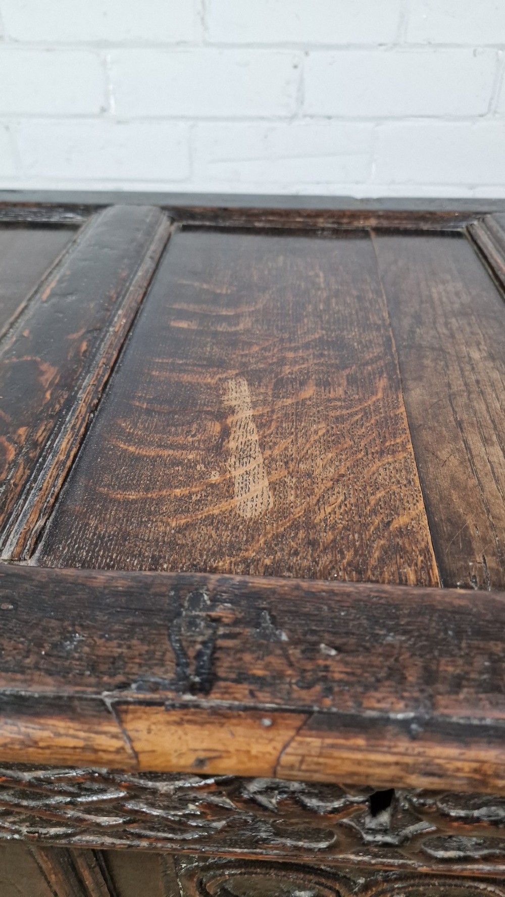 A late 17th-century dark oak coffer with a hinged lid, featuring three carved front panels and an intricate carved top frieze. View IV