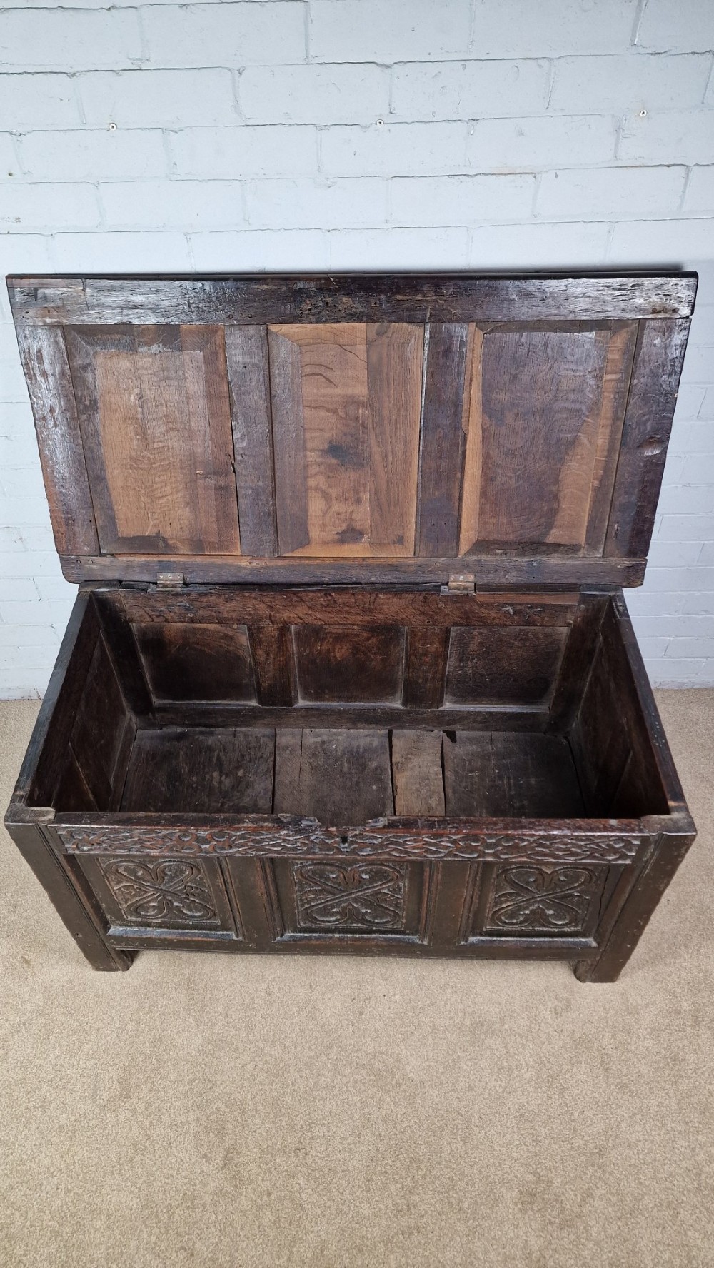 A late 17th-century dark oak coffer with a hinged lid, featuring three carved front panels and an intricate carved top frieze. View V