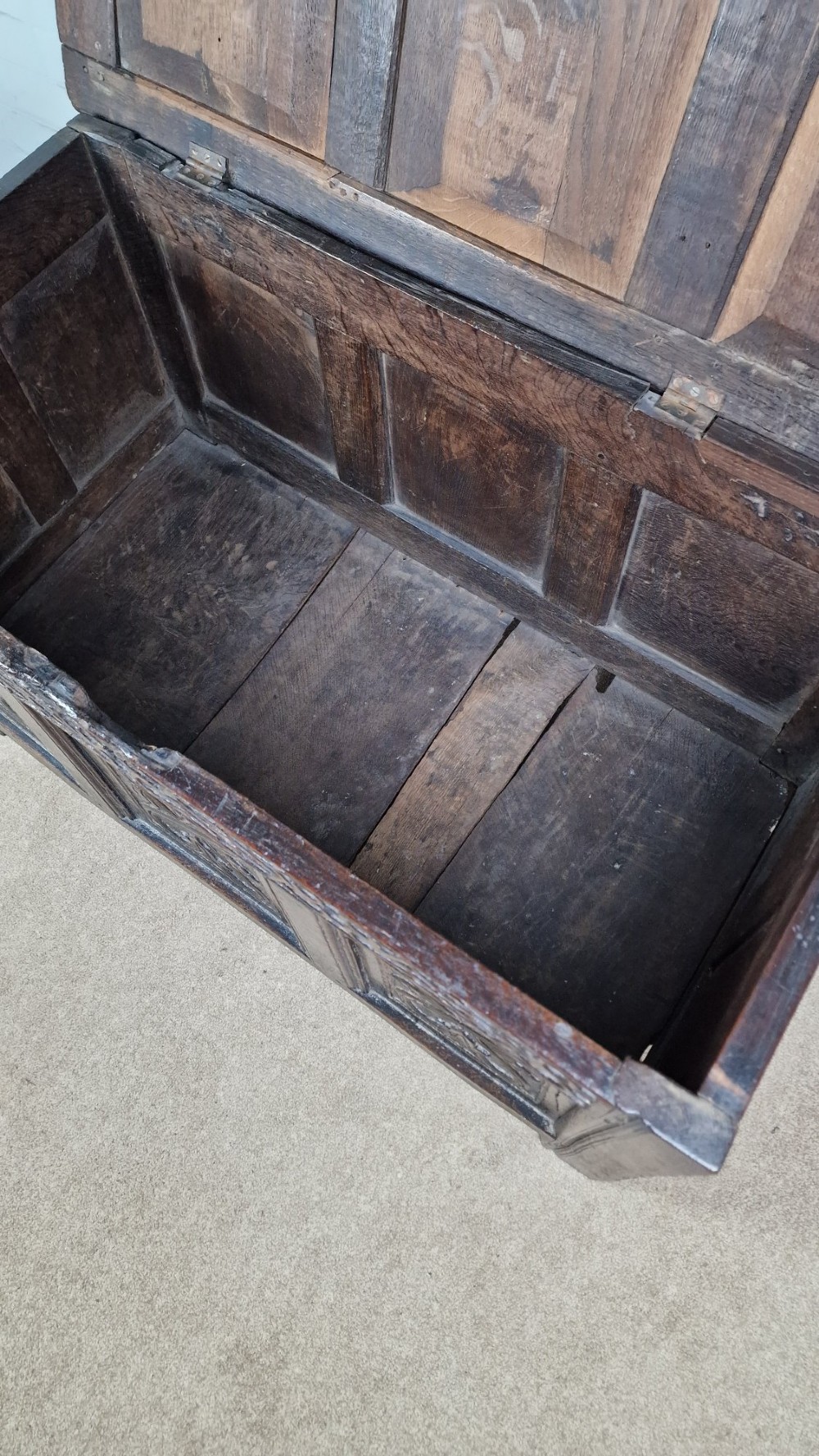 A late 17th-century dark oak coffer with a hinged lid, featuring three carved front panels and an intricate carved top frieze. View VI