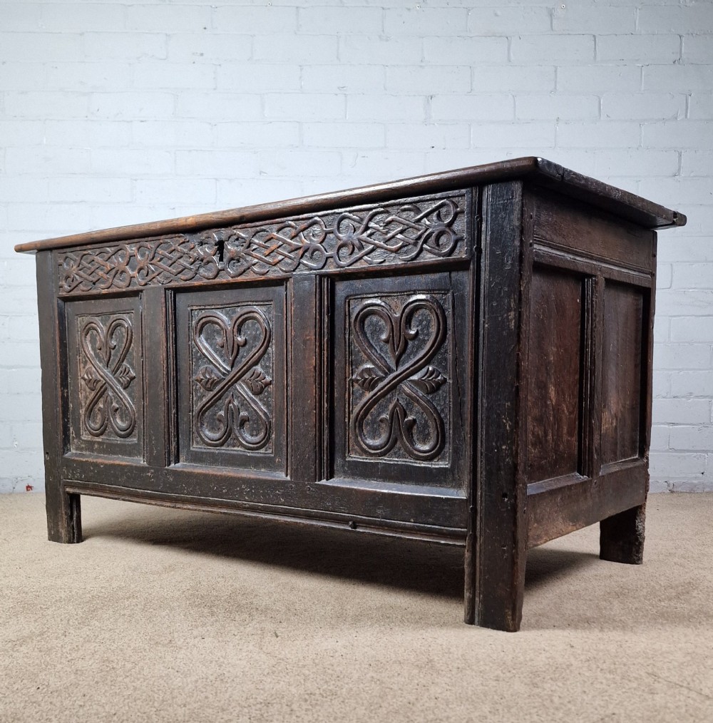 A late 17th-century dark oak coffer with a hinged lid, featuring three carved front panels and an intricate carved top frieze. View VII