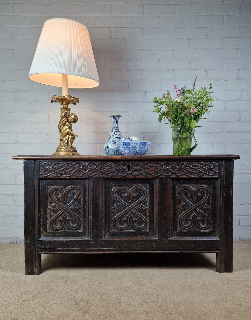A late 17th-century dark oak coffer with a hinged lid, featuring three carved front panels and an intricate carved top frieze.