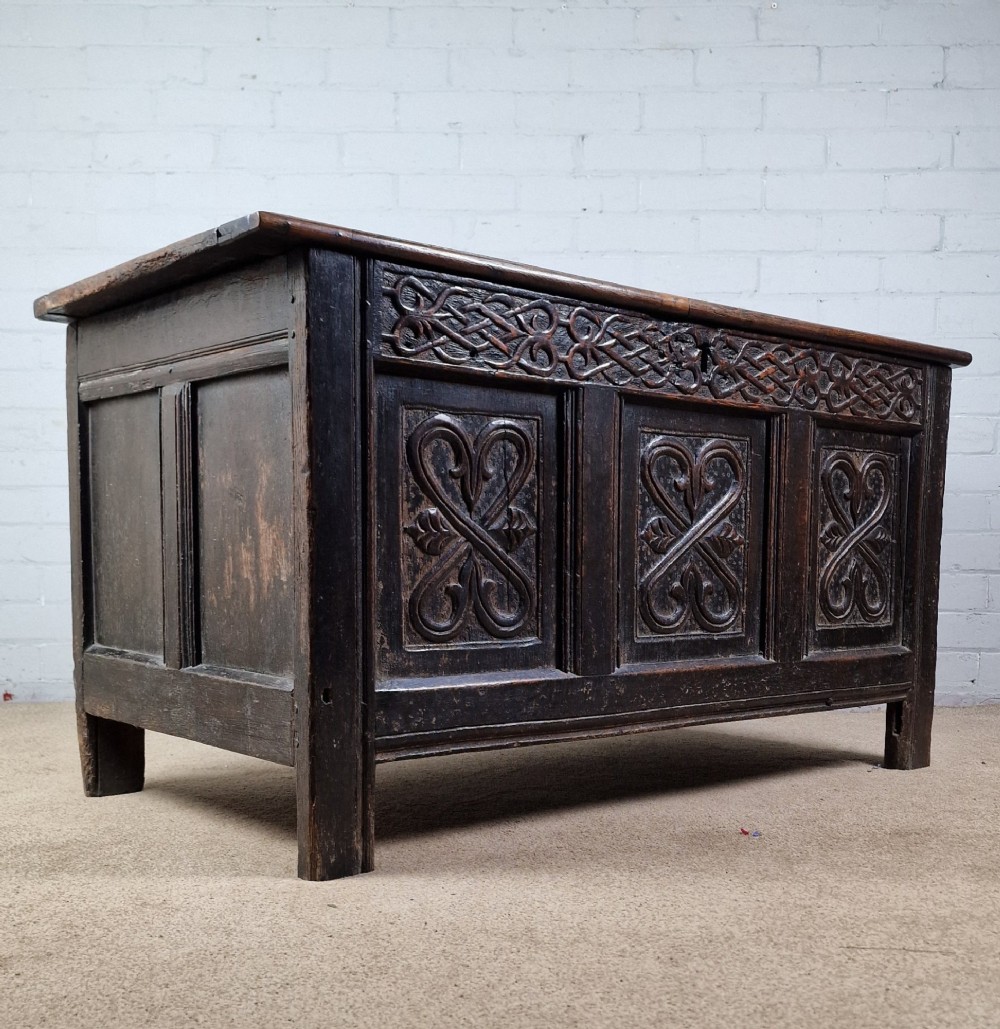 A late 17th-century dark oak coffer with a hinged lid, featuring three carved front panels and an intricate carved top frieze. View VIII