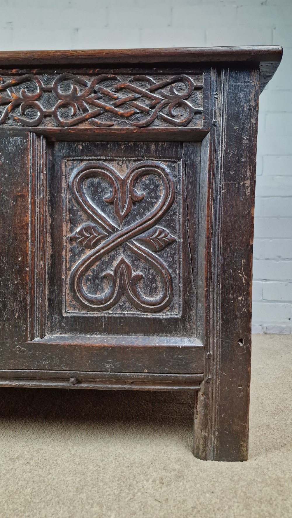 A late 17th-century dark oak coffer with a hinged lid, featuring three carved front panels and an intricate carved top frieze. View X