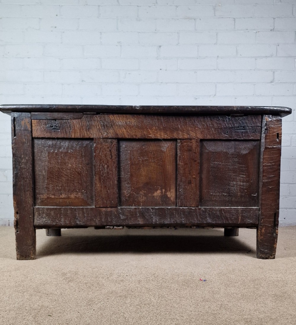 A late 17th-century dark oak coffer with a hinged lid, featuring three carved front panels and an intricate carved top frieze. View XI