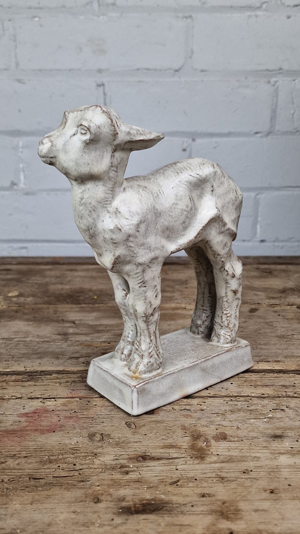 A cream glazed terracotta figurine depicting a standing kid goat mounted on a low rectangular base. View IV