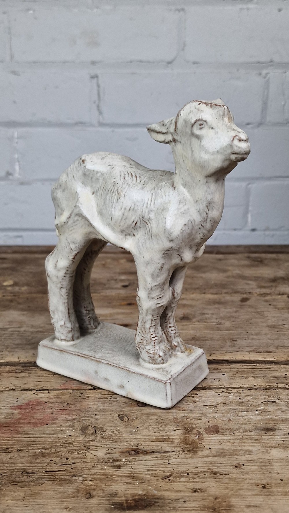 A cream glazed terracotta figurine depicting a standing kid goat mounted on a low rectangular base.
